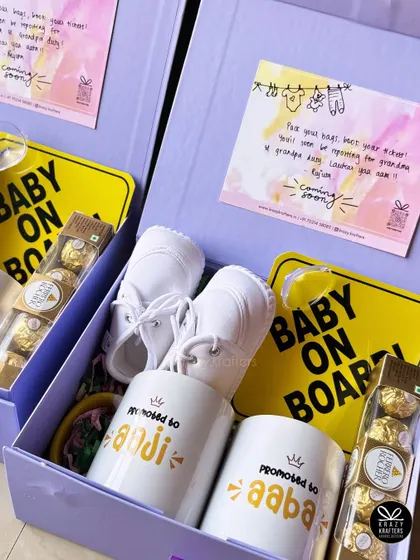 Two beautiful lavender-themed boxes ready to go out for a pregnancy announcement, complete with 'Baby on Board' signs and personalized mugs for 'Aaji' and 'Aaba'.