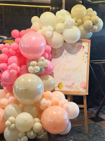 A beautiful welcome sign for a second birthday, nestled in a stunning organic balloon garland of pink, peach, and white. Butterfly details add a touch of whimsy.