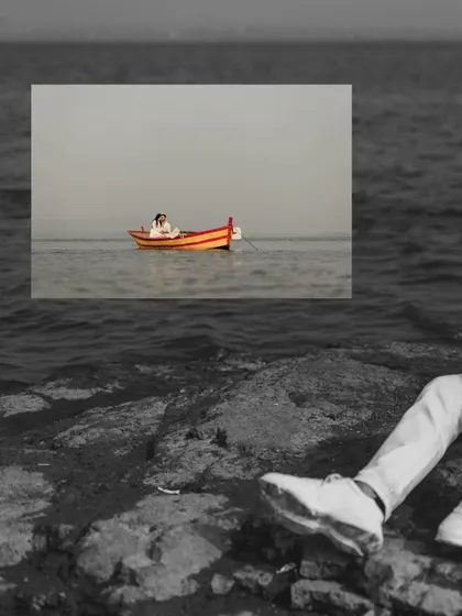 An artistic shot of the couple in a boat, framed by the rocky shore in the foreground. The black and white on the rocks makes the colorful boat pop.