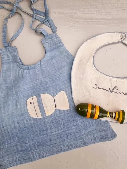Another variation of our newborn gift set, this one features a fish applique on a blue hand-dyed Kora cotton dress, paired with a matching Channapatna fish rattle. It's a perfect example of creative collaboration.