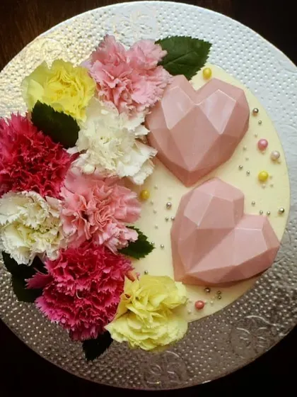 A top-down view of the anniversary cake, showing the beautiful arrangement of fresh carnations and geometric hearts. The combination of textures and colors makes it truly special.