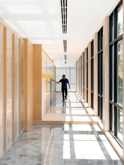 Natural light floods this hallway through large windows, creating a play of light and shadow on the textured wall panels. This interaction with light changes the feel of the space throughout the day.