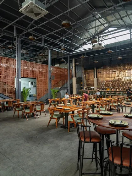 This wide-angle view showcases the scale of the double-volume dining space and two of our signature elements. The rustic terracotta partition wall adds warmth and texture while screening private areas, contrasting beautifully with the industrial metal and concrete surfaces of this modern pub interior.