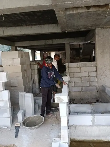 Workers laying AAC blocks for interior walls. This phase of construction begins to define the individual rooms and spaces within the building's main frame.