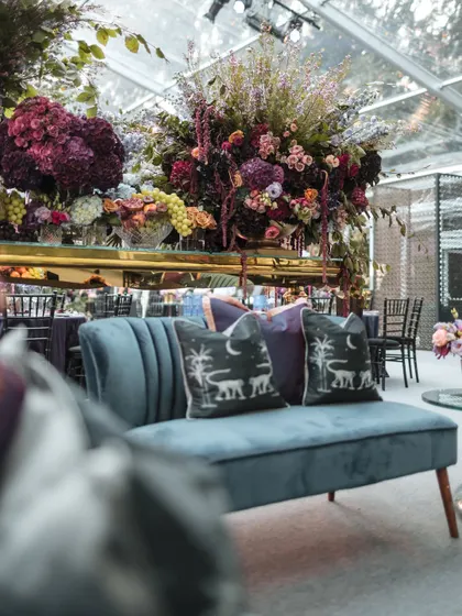 Interior shots of the Bridgerton-themed Sangeet, highlighting the moody lighting, rich velvet furniture, and dramatic floral centerpieces.