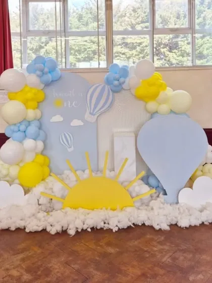 A dreamy "Up, Up and Away" theme for a first birthday, using soft blue and yellow balloons, cloud cutouts, and hot air balloon props to create a whimsical sky scene.