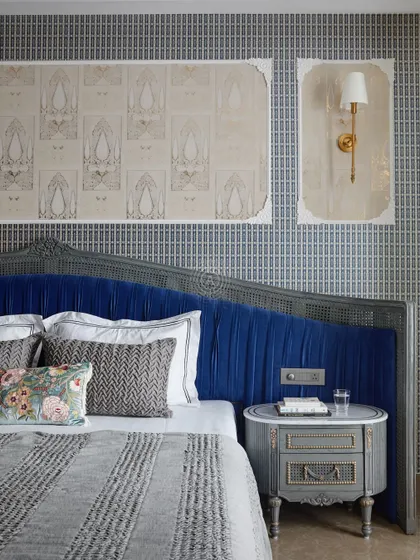 A close-up of the bed, showing the intricate floral embroidery on the cushion and the detailed carving on the headboard. The mix of patterns and textures creates a rich, layered look.
