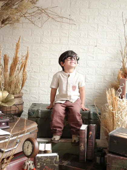A little gentleman and a scholar. This vintage-themed shoot features a young boy with glasses, smiling happily while sitting on old trunks surrounded by books and a gramophone.