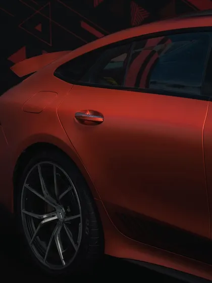 A close-up on the rear quarter panel and door handle of a matte orange Mercedes-AMG. The lighting is used to accentuate the car's muscular curves and unique paint finish.