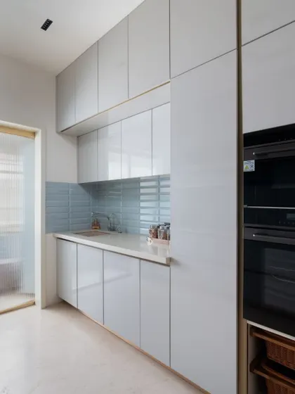 A clean and minimalist utility kitchen, featuring floor-to-ceiling storage and a calming blue backsplash.