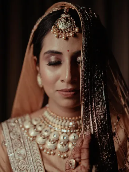 A close-up portrait of a bride in a soft peach lehenga, her expression serene and beautiful, showcasing her elegant jewelry.