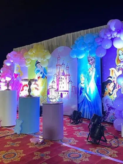 A full view of an outdoor princess party stage, with multiple princess backdrops and a large light-up number '1'.