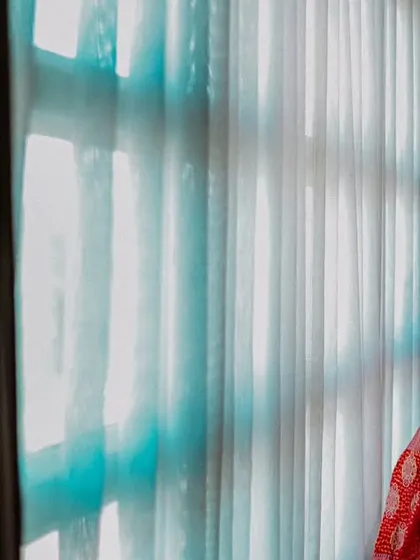 A smiling bride by the window, her red and pink lehenga glowing in the natural light.