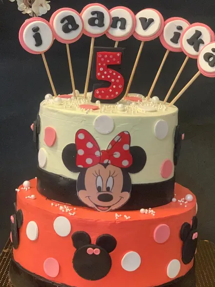 A cheerful two-tier Minnie Mouse cake for a 5th birthday. The classic red and black polka dot design is topped with a personalized name banner.