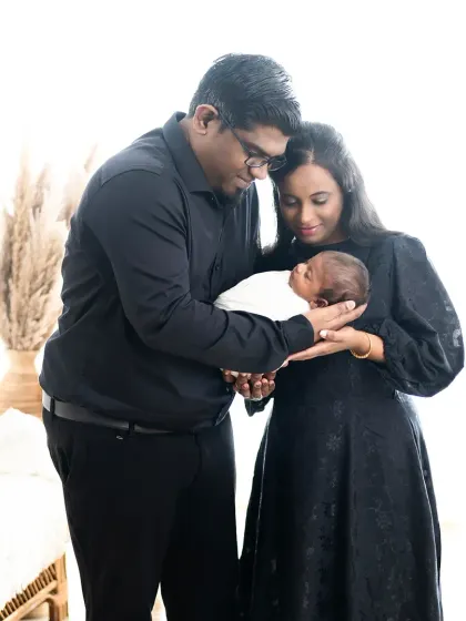 A beautiful silhouette-style portrait of new parents holding their baby. The soft, natural light from the window creates a gentle and intimate mood.
