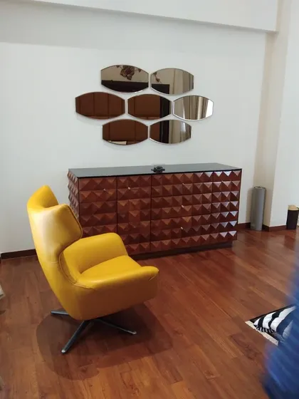 A stylish reading or seating nook featuring a modern yellow swivel armchair and a unique sideboard with a 3D geometric pyramid pattern. The wall is adorned with a cluster of hexagonal mirrors, adding a touch of artistic flair.
