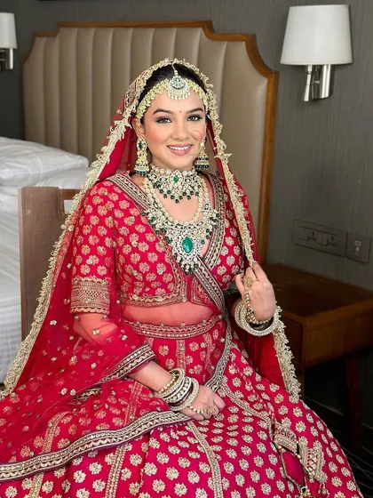 A radiant bride in a classic red and green lehenga. The makeup is timeless, with defined eyes and a warm lip color that complements the rich tones of her outfit.
