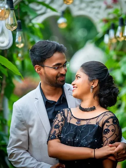 A lovely portrait of a couple framed by lush greenery and hanging lights, creating a magical, romantic atmosphere.