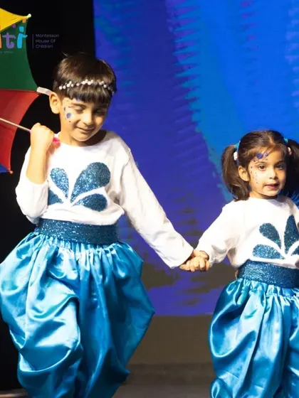 Two children hold hands and dance together during the Neera performance, their smiles lighting up the stage.