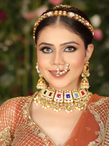 A close-up bridal beauty shot, focusing on the model's flawless makeup, navratna-style necklace, and elegant matha patti.