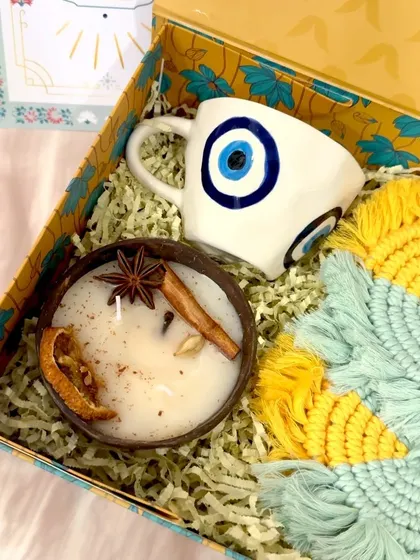 This "Nurture and Protection" hamper is a unique take on Diwali gifting. It features a ceramic evil eye mug, a fragrant coconut shell candle with spices, and handmade macrame coasters, all nestled in a designer box.