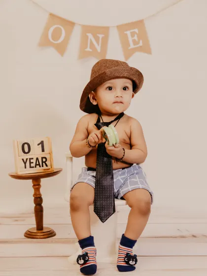 A baby boy in a hat and tie sits for his "01 Year" photo in the studio.