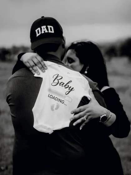 A touching black and white photo of the couple embracing, with a "Baby Loading" onesie on the dad's back. It’s a cute, modern, and heartfelt announcement.