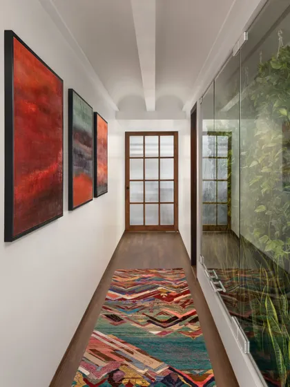 This passage in the West Coast Residence features a glass wall on one side, which enclosures a small green space, bringing a surprising element of nature into the heart of the apartment.