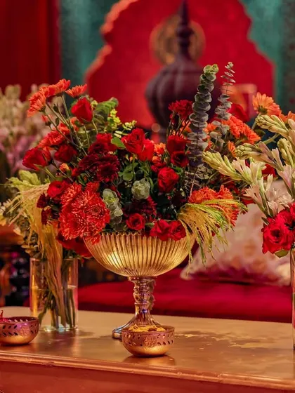 A close-up of a floral arrangement on a coffee table in the lounge area. The vibrant red flowers pop against the deep red velvet sofa, creating a rich, monochromatic color story.