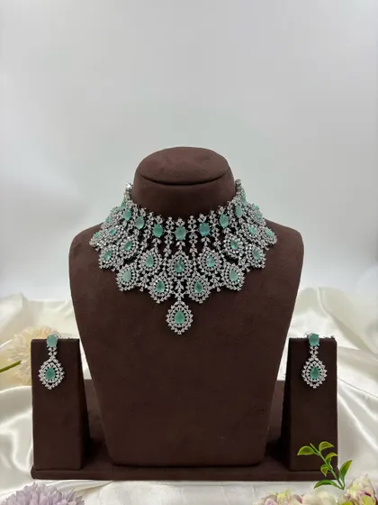 A heavy, silver-plated AD necklace set with a peacock-inspired feather design. This statement piece is available in blue, green, pink, and all-white.