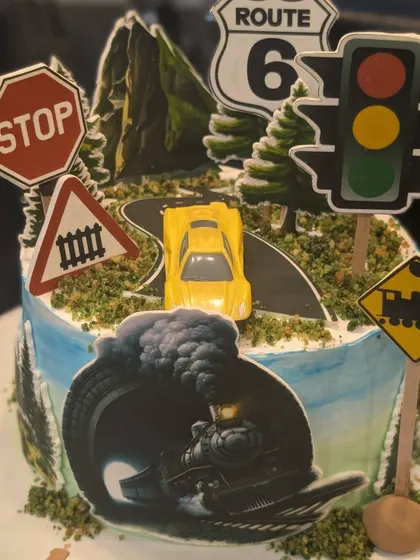 A fun road trip themed cake. It's decorated with a toy car on a winding road, surrounded by edible images of traffic signs and a train.
