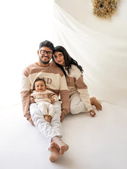 A beautiful family portrait with everyone in matching color-blocked sweaters. The coordination adds a lovely touch to this clean, modern studio photo.