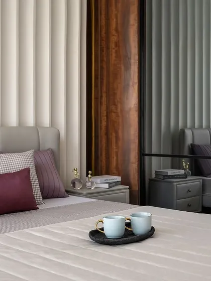 Texture is key in this serene bedroom. We used a vertically fluted panel behind the bed, paired with a grey upholstered headboard. The color palette of mauve, plum, and grey, combined with mirrored wardrobe doors, creates a space that feels both soft and spacious.