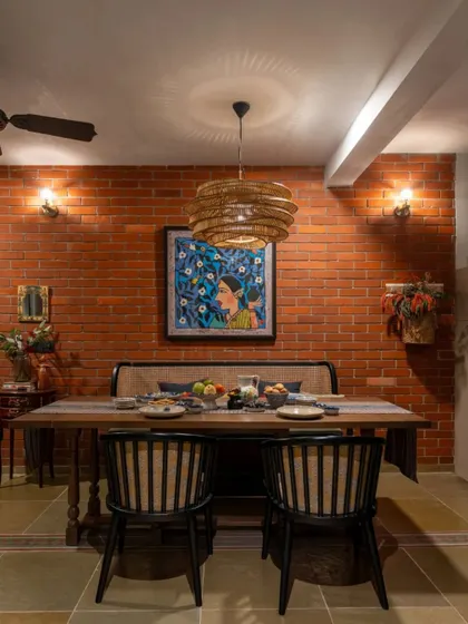 The dining nook in the Dhaka residence, set against a warm brick wall. The space feels intimate and cozy, perfect for family meals. The woven pendant light and modern chairs add a contemporary touch to the rustic backdrop.
