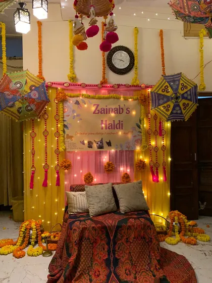 The complete home Haldi setup with a decorated seating area, a personalized banner, and colorful umbrellas. This shows how even a small space can be made perfect for celebrations.