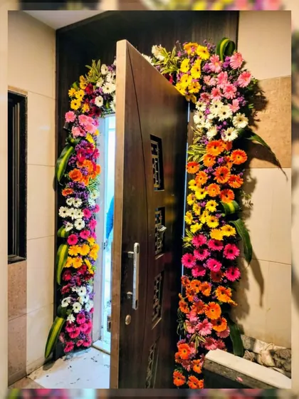A burst of color to welcome guests. This door arch is crafted with a vibrant mix of gerbera daisies in shades of orange, pink, yellow, and white, making for a cheerful and lively entrance.