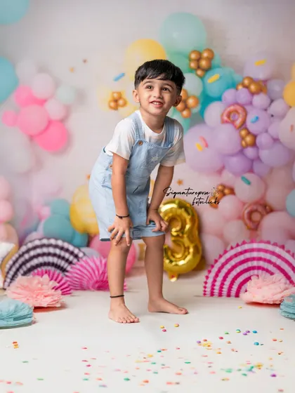 A candid moment of joy from a third birthday photoshoot. The colorful confetti on the floor and the cheerful balloon arrangement create a lively party atmosphere right here in the studio.