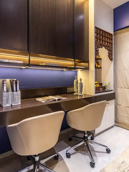 This before-and-after shows the transformation of a cluttered corner into a sophisticated dual-person workspace. The deep blue wall, warm wood tones, and integrated Mandir create a space that is both productive and peaceful.