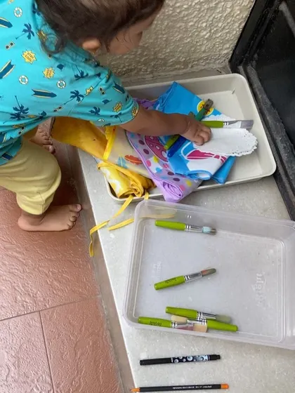 A toddler helps put paintbrushes away after an art session. Involving children in the clean-up process gives them a sense of accomplishment and ownership over their space.