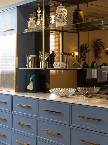 A close-up of the custom-designed crockery unit, featuring a tinted mirror back, glass shelves, and a beautiful dusty blue finish.
