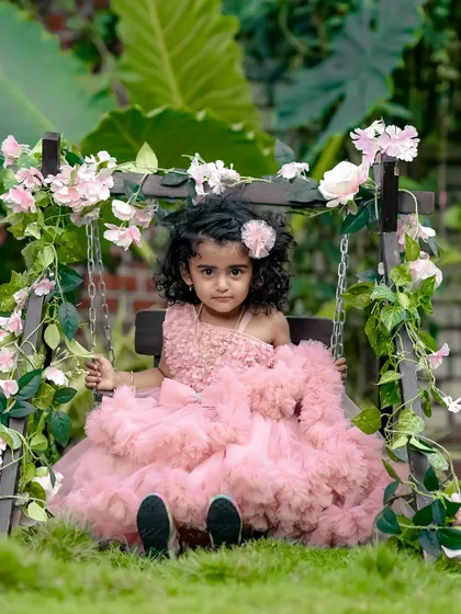 A classic portrait of a little girl in a stunning pink dress on our floral swing, set against the beautiful greenery of our garden.
