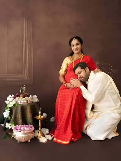 A tender moment during a traditional maternity photoshoot. The husband-to-be listens to the baby bump, set against a classic, painterly backdrop, blending cultural elegance with heartfelt emotion.