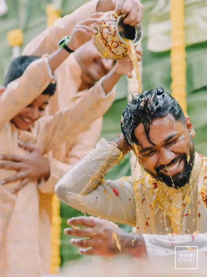 A close-up of the groom laughing as he's doused with turmeric water. This candid shot perfectly captures the unrestrained happiness of the moment.