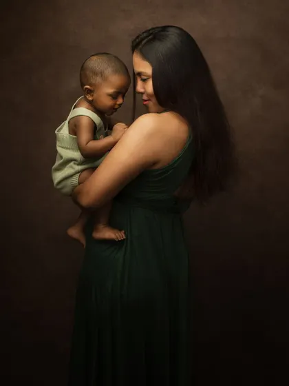 A tender moment between mother and child. The soft lighting and dark backdrop create an intimate and emotional fine art portrait.