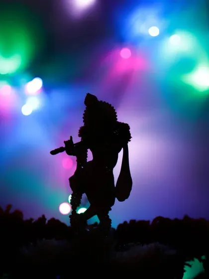 The silhouette of a Krishna idol is set against a vibrant, colorful background of bokeh lights. This creative shot combines religious iconography with modern photographic techniques.