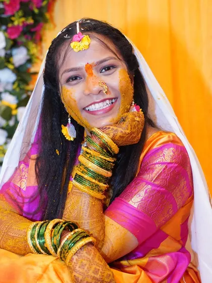A joyful portrait of the bride with haldi on her face, smiling brightly.