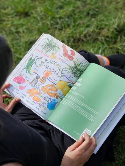 Someone reading the beautifully illustrated coriander chutney recipe in a park.