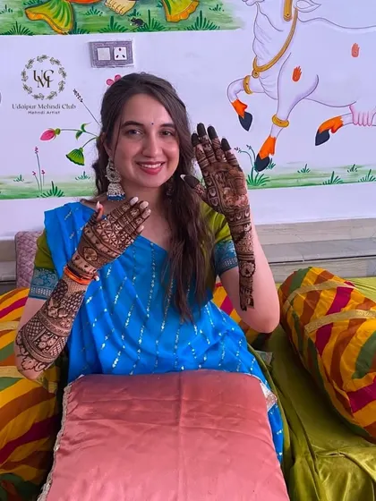 A happy bride showing off her freshly applied mehndi. The design includes a beautiful portrait of a couple.
