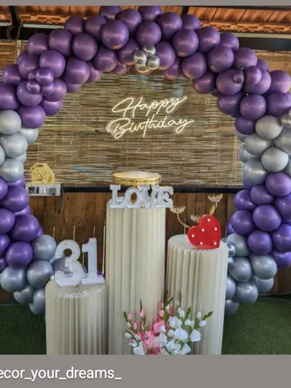 A 31st birthday party with a purple and silver balloon arch against a rustic bamboo wall.