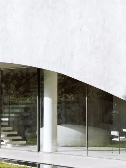 The minimalist glass facade of Villa KD 45, which allows for uninterrupted views of the garden. The floating staircase inside is visible, adding a touch of sculptural elegance to the interior.